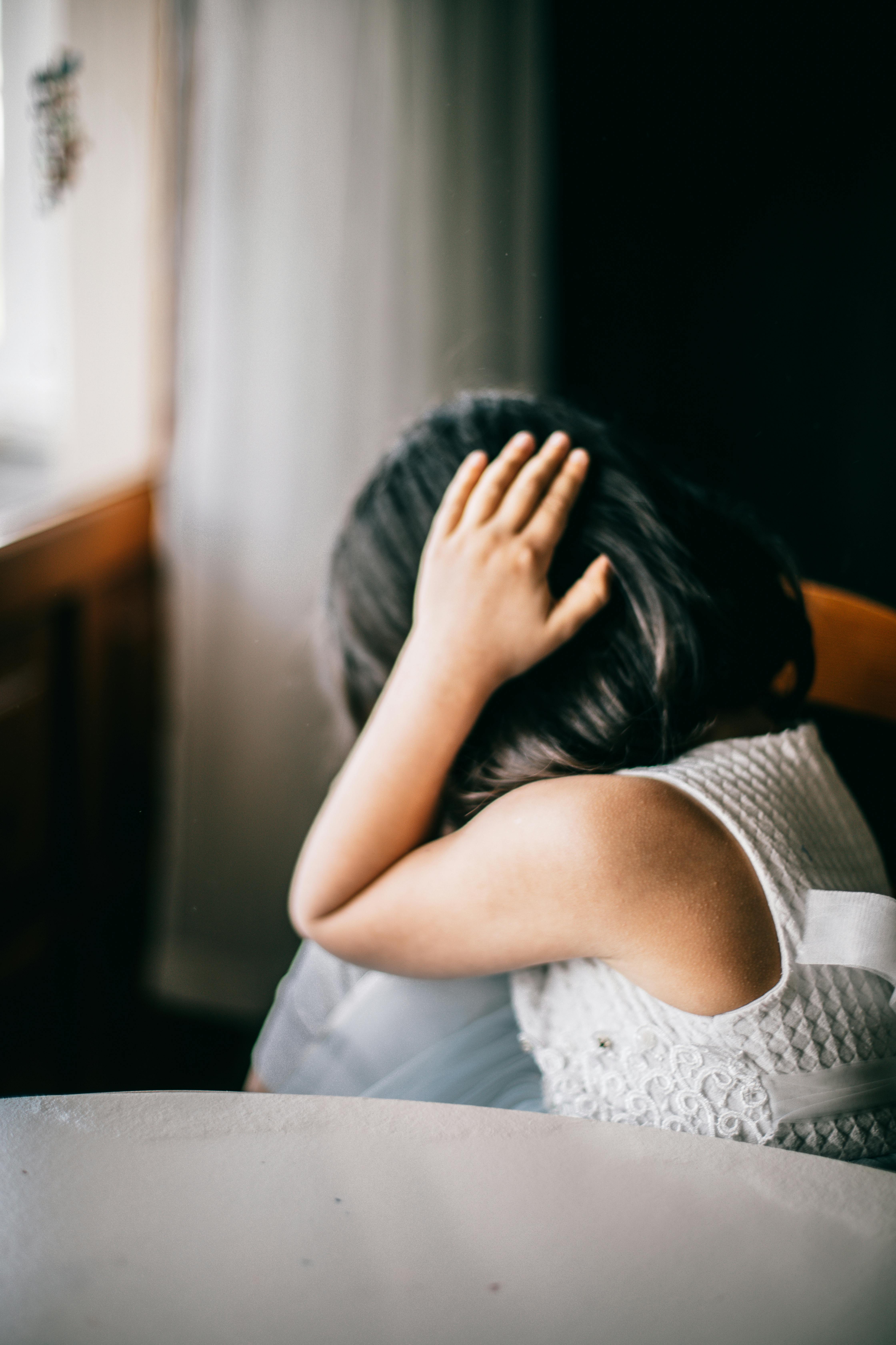 Woman sitting by a window with her head in her hand, symbolizing stress, anxiety, and emotional distress.
